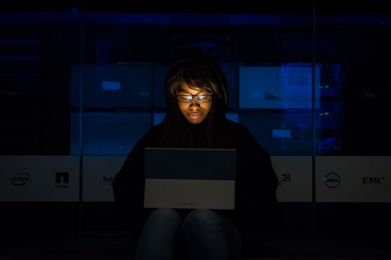 who-we-are A woman uses her laptop in a dimly lit server room, focusing on technology and work.